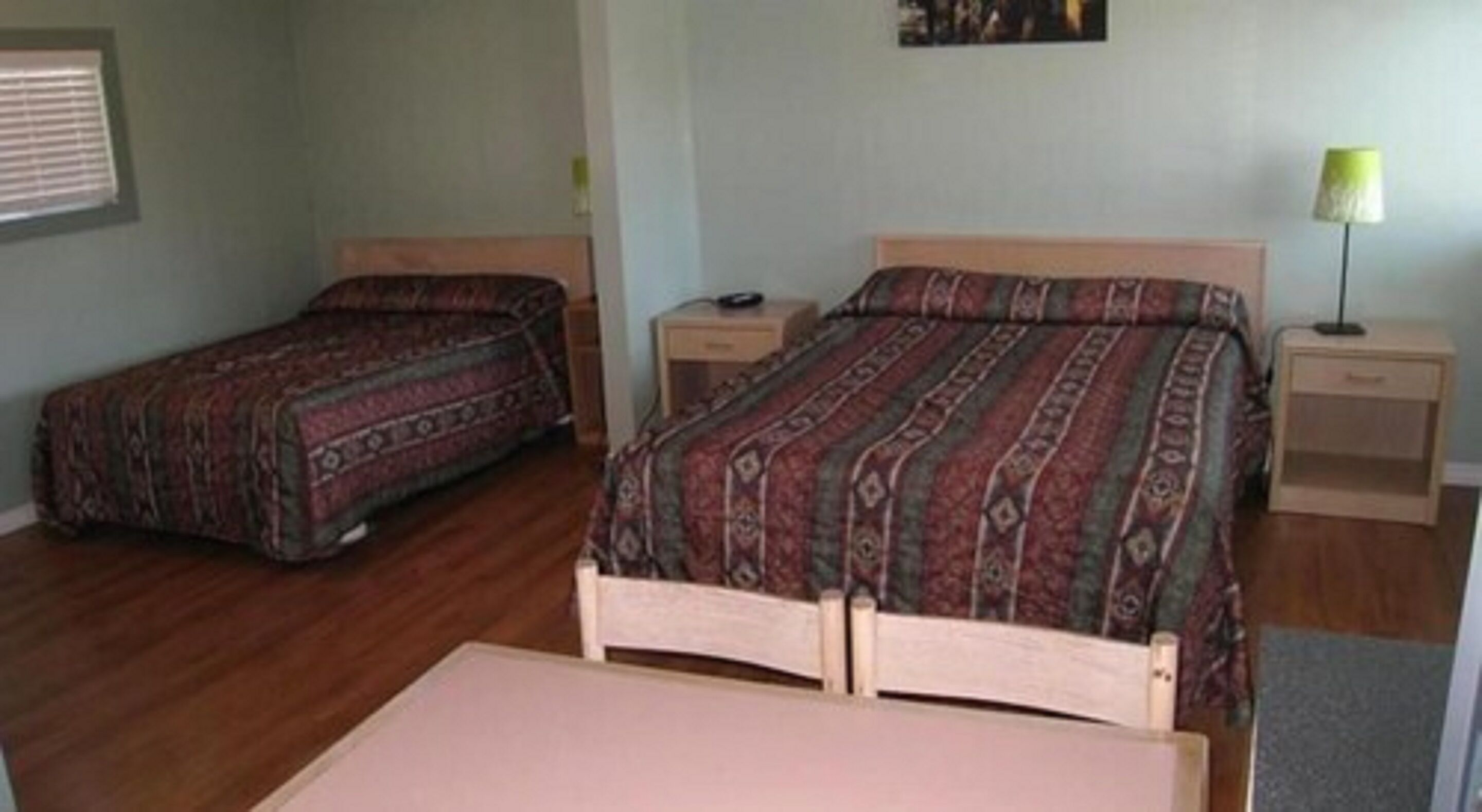 A room with two single beds, a small table, and a nightstand with a lamp.