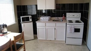A compact kitchen with white cabinets, a microwave, a toaster, a sink, and a stove. - Beach Grove Motel (Delta)