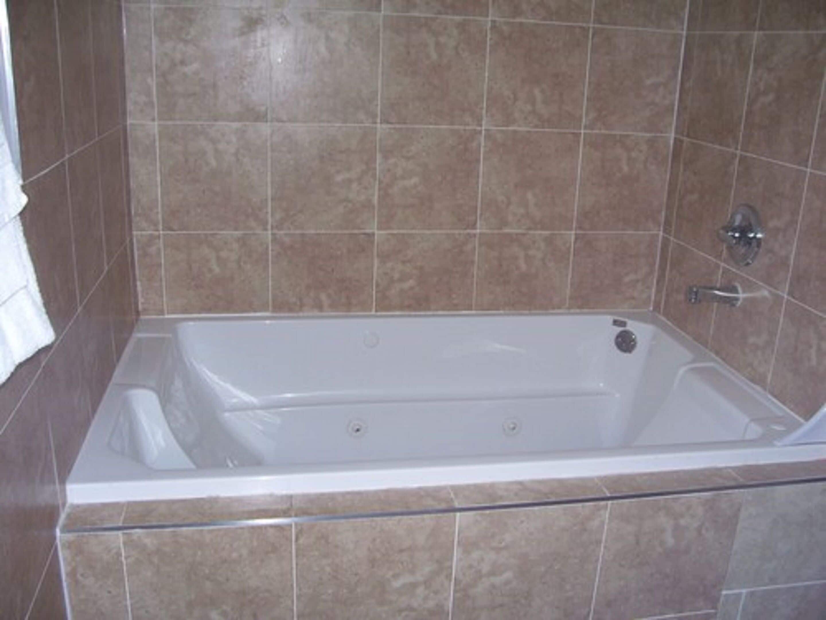 Une baignoire rectangulaire standard, dotée d’un robinet et d’une molette de réglage, placée devant un mur carrelé.