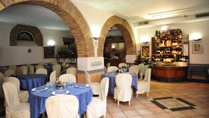 Restaurante com arcos de tijolo, mesas redondas com toalhas azuis e um espaço de bar com adega.