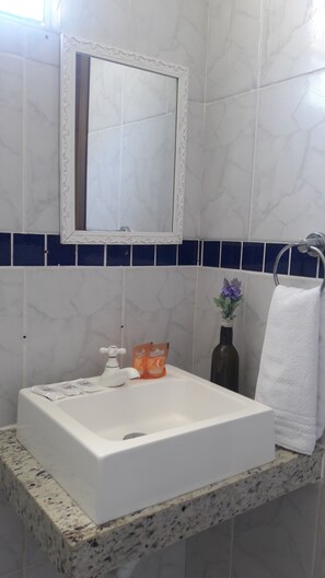 Un baño con lavamanos blanco, espejo, toallero y una pequeña planta en maceta.