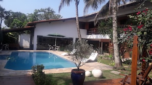 A swimming pool with lounge chairs, a patio area, and a house with a garden. - Pousada Mari (Guarujá)