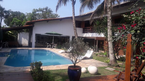 Una piscina con sillas de descanso, un patio y una casa con jardín.