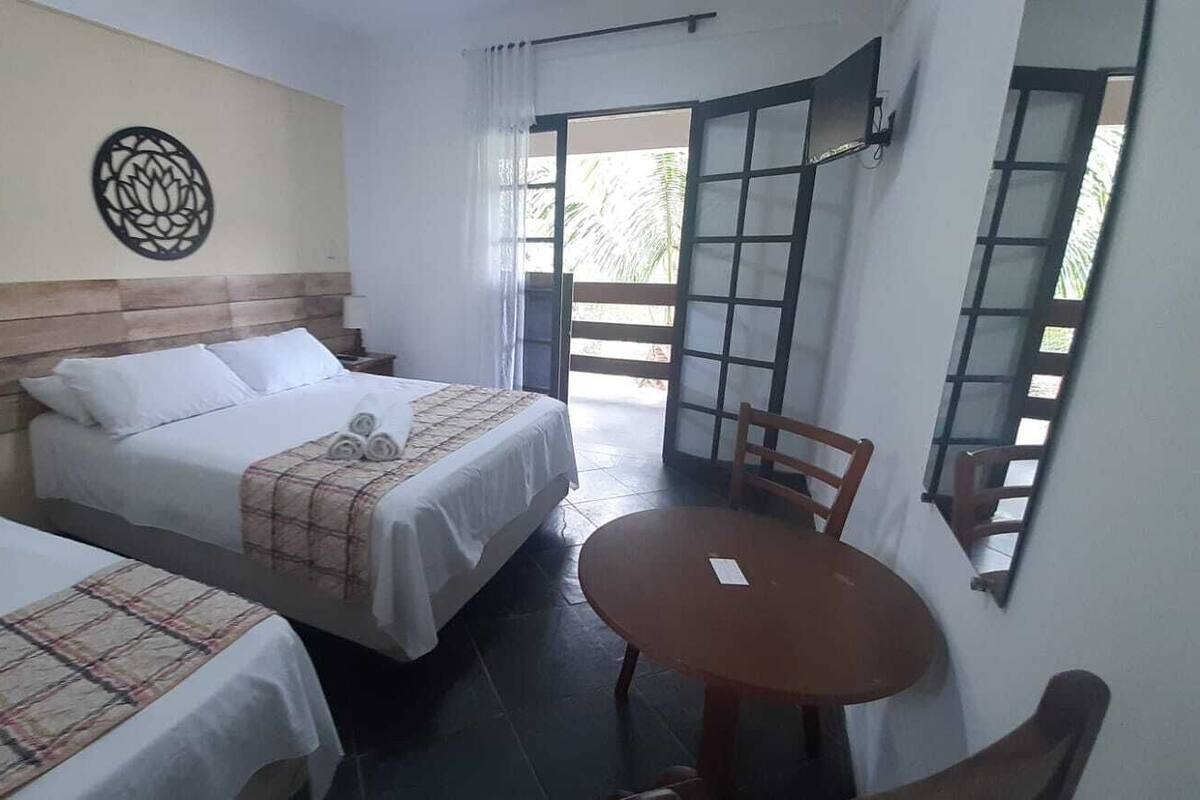 Habitación de hotel con dos camas, una mesita y vistas al exterior.