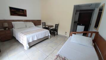 A hotel room with a bed, a small table with two chairs, a dresser, and a painting on the wall.