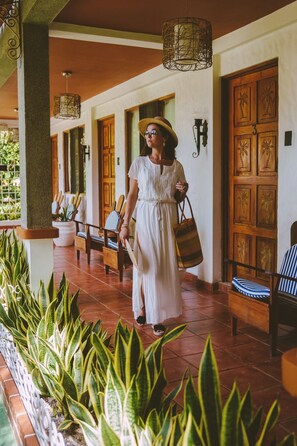 A person walking through a covered outdoor area with wooden doors and chairs. - Hotel Villabosque Eco Boutique (Quepos)