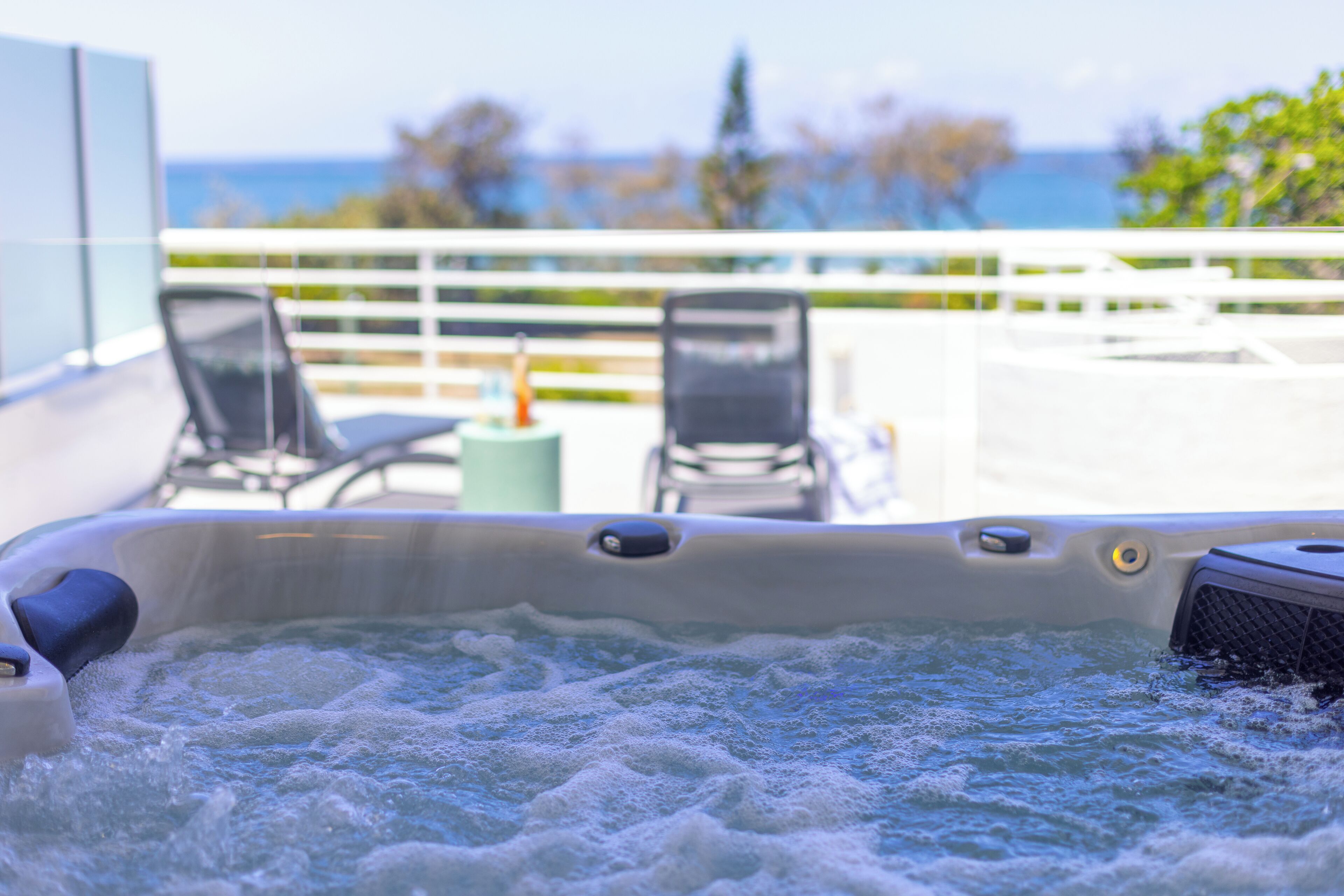 Un jacuzzi con vista al océano y sillas en un balcón.