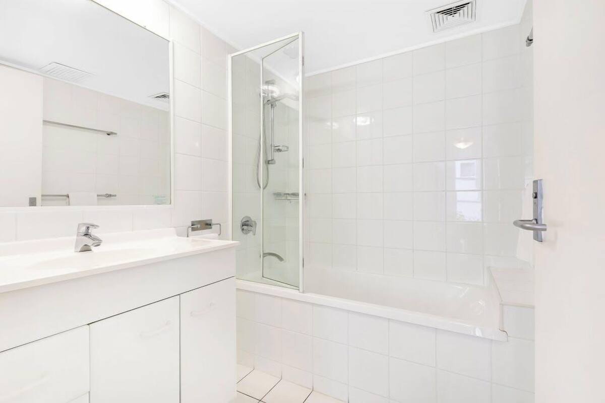 A modern bathroom with a white sink, mirror, and glass-enclosed shower.
