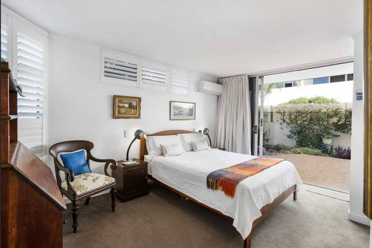 A bedroom with a bed, a chair, a nightstand, and a window with blinds.