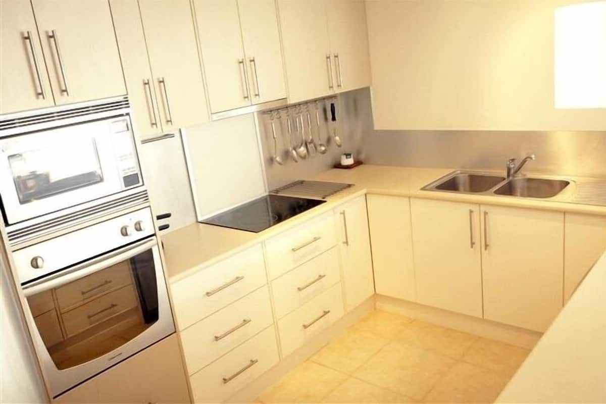 A kitchen with white cabinets, a microwave, an oven, a sink, and hanging utensils.