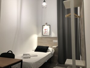 A hotel room with a single bed, a desk, a chair, a hanging light fixture, and a framed picture on the wall.