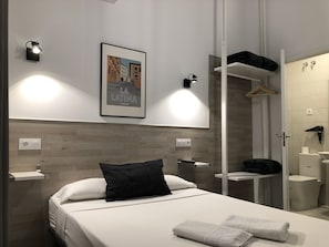 A modern hotel room with a bed, a nightstand, a framed picture on the wall, a wardrobe, and a bathroom with a toilet and sink.