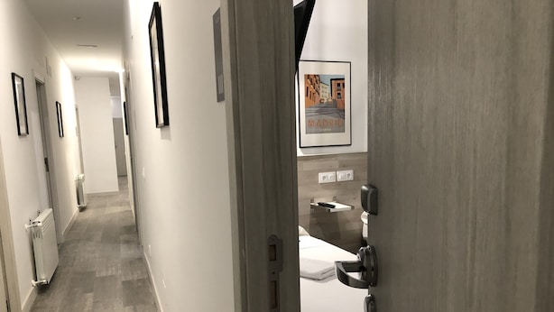 A hotel corridor with a bed, a bathroom with a toilet, and a framed picture on the wall. - Hostal Rias Bajas (Madrid)
