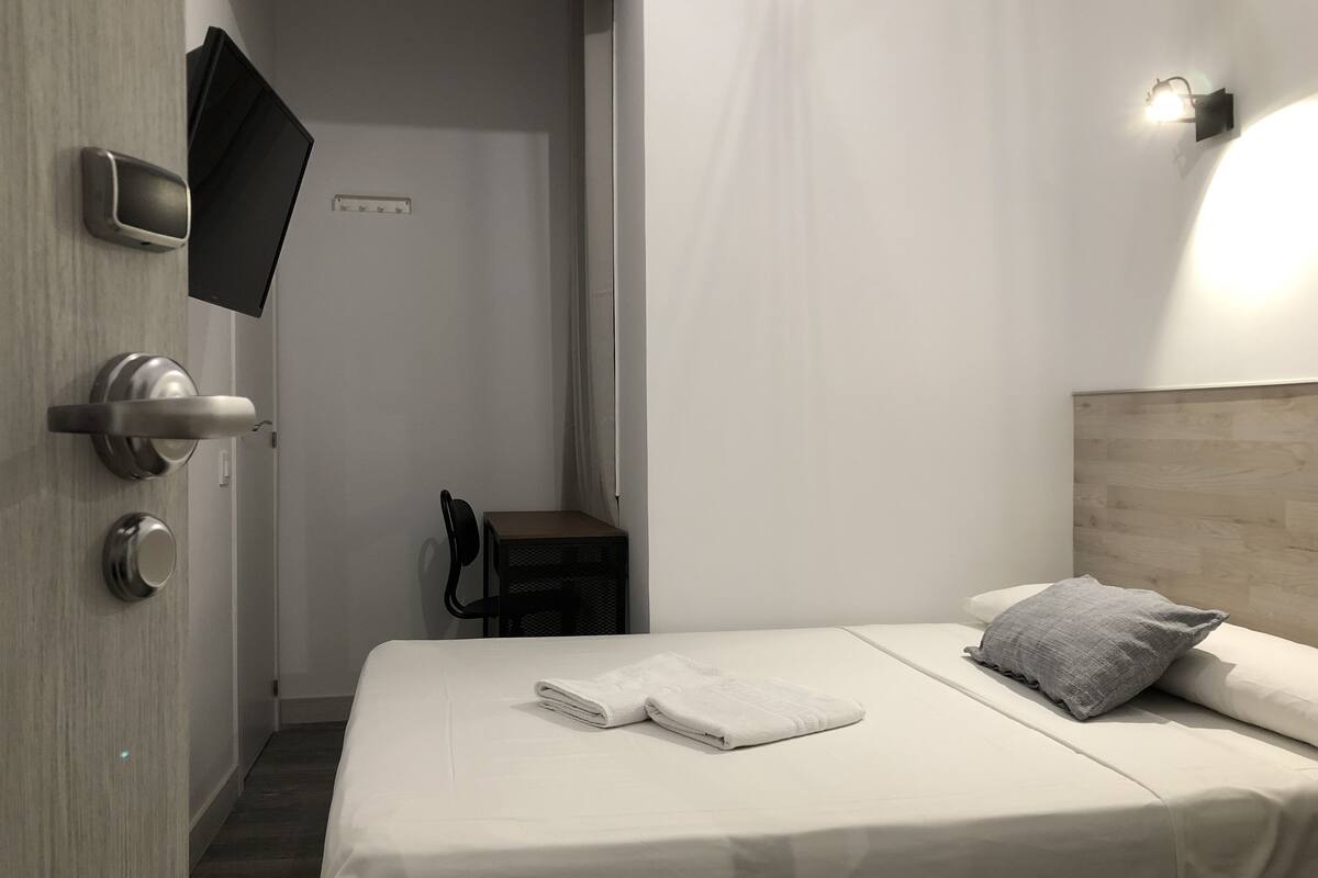 A modern hotel room with a bed, a TV mounted on the wall, a small table, and a chair.