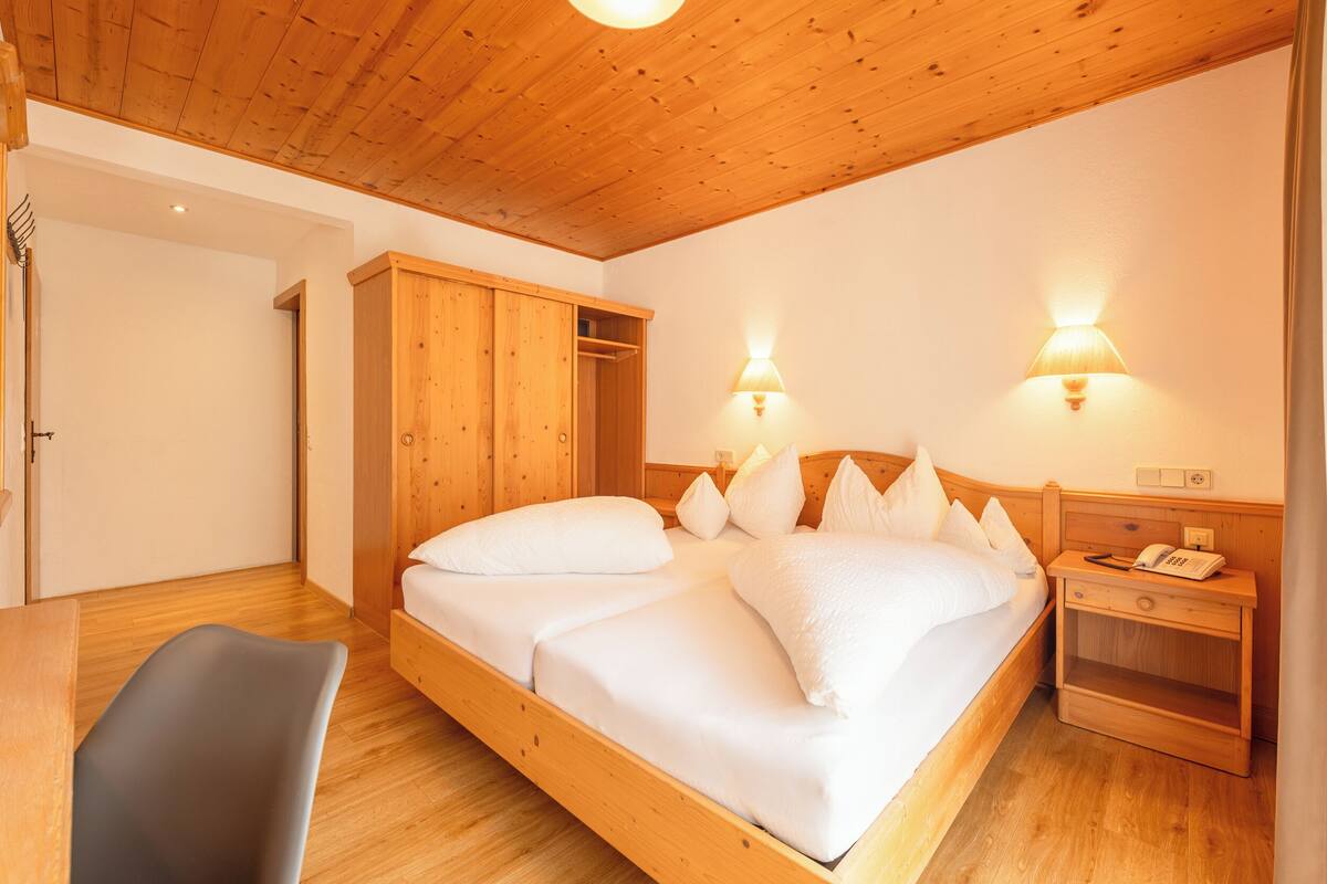 A wooden-framed bedroom with a bed, bedside lamps, and a nightstand.