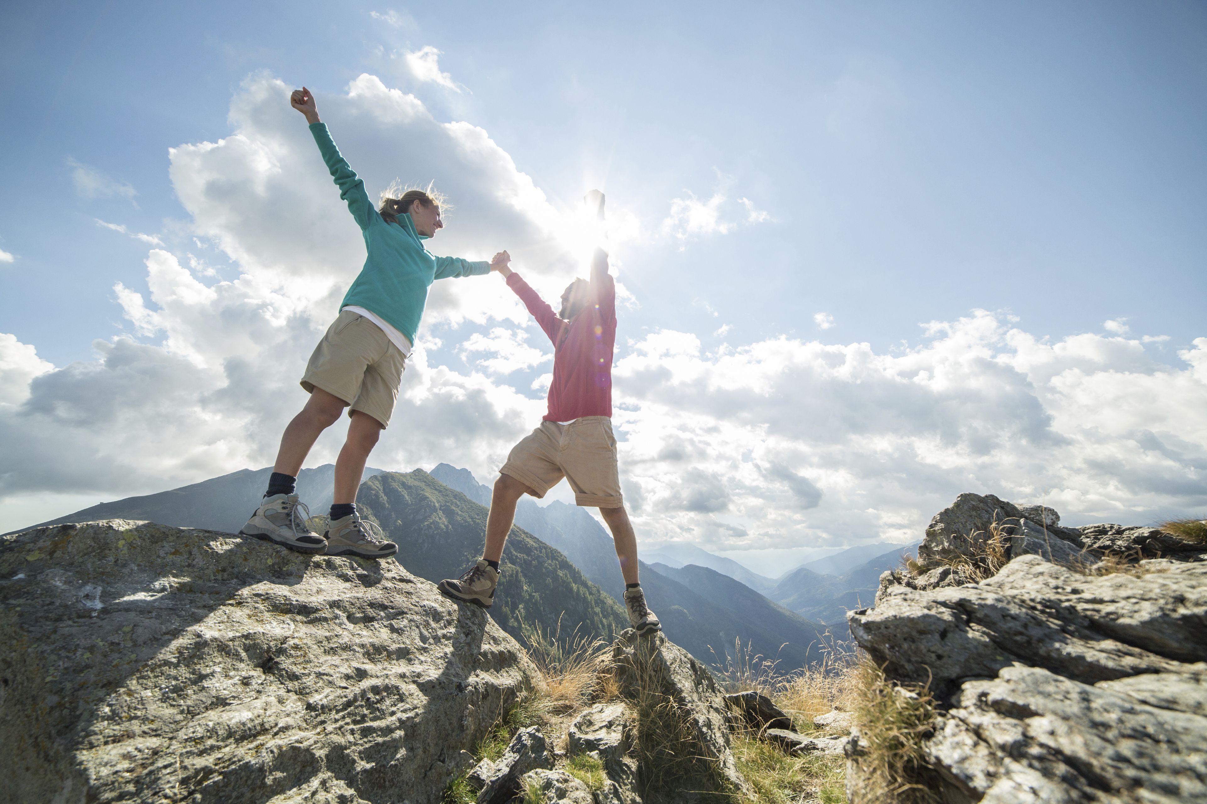 Two people standing on a rocky mountain peak with a clear sky and distant mountains in the background.