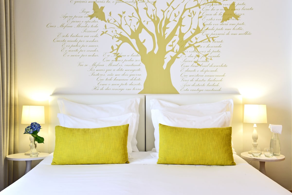 A hotel room with a bed, two pillows, a nightstand with a lamp, and a wall decoration.