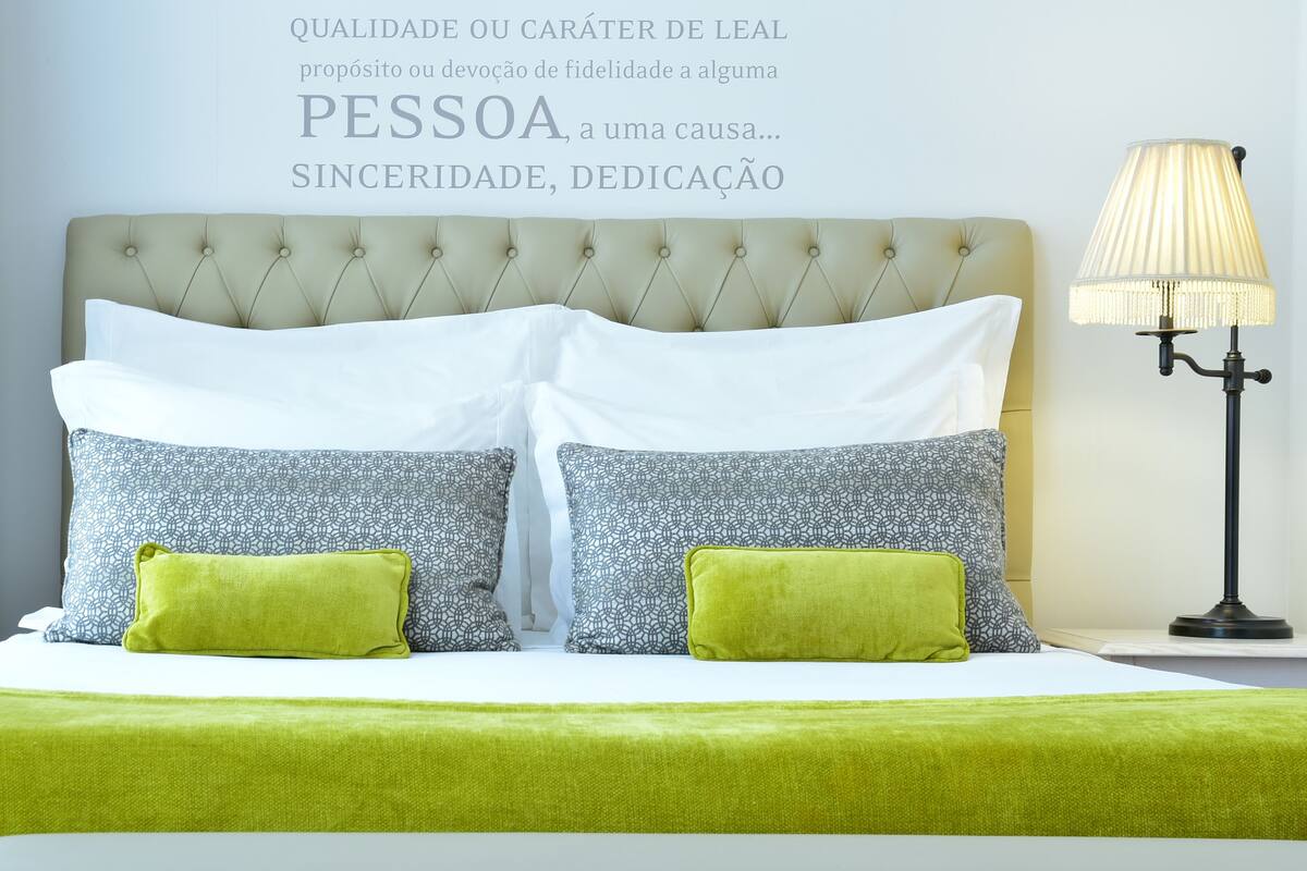 A neatly made bed with a tufted headboard, two patterned pillows, and a green throw.