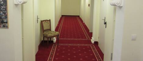 A hallway with a red carpet, white walls, and a chandelier.