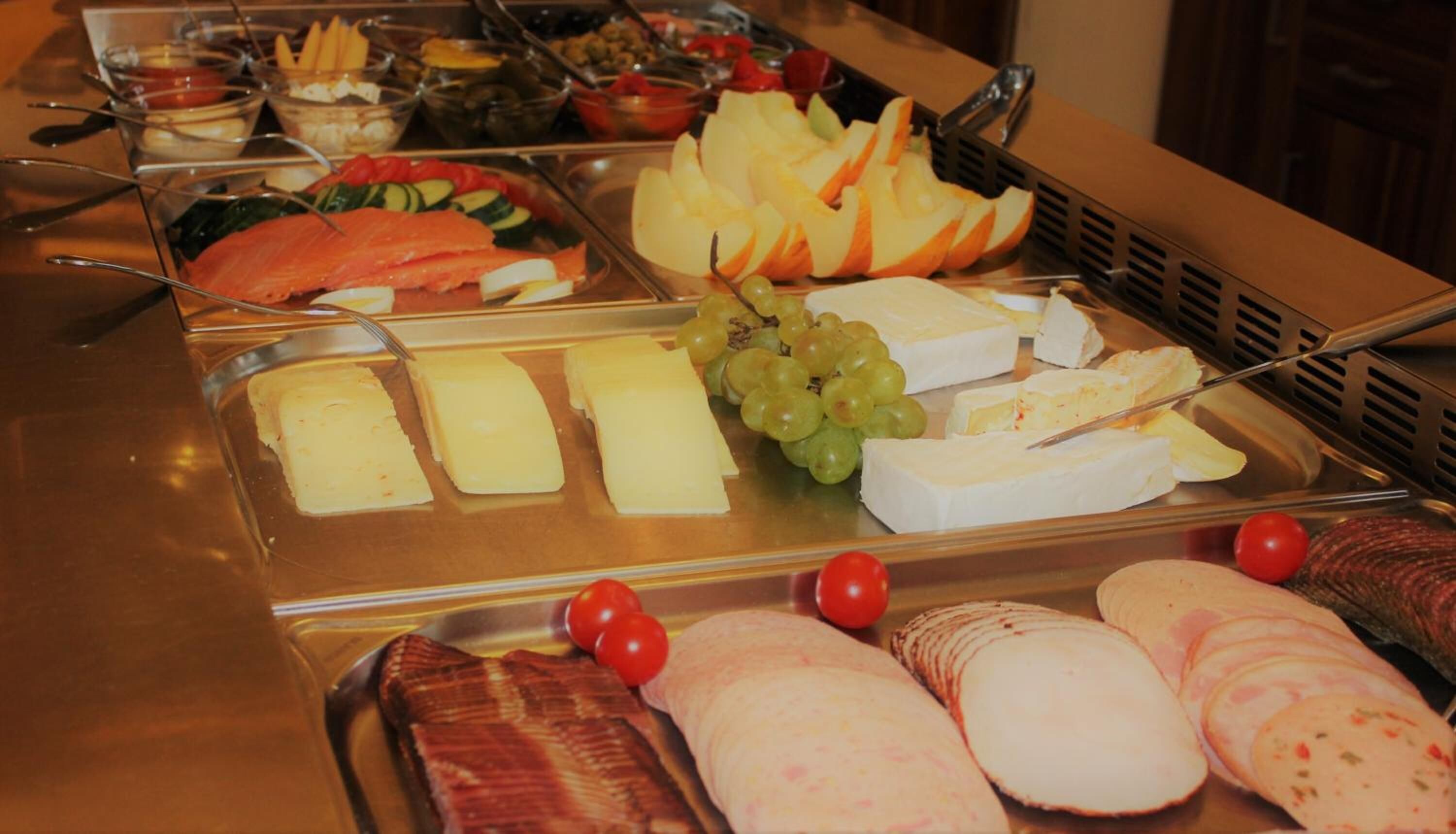 A buffet with various food items including salmon, cheese, grapes, and tomatoes.