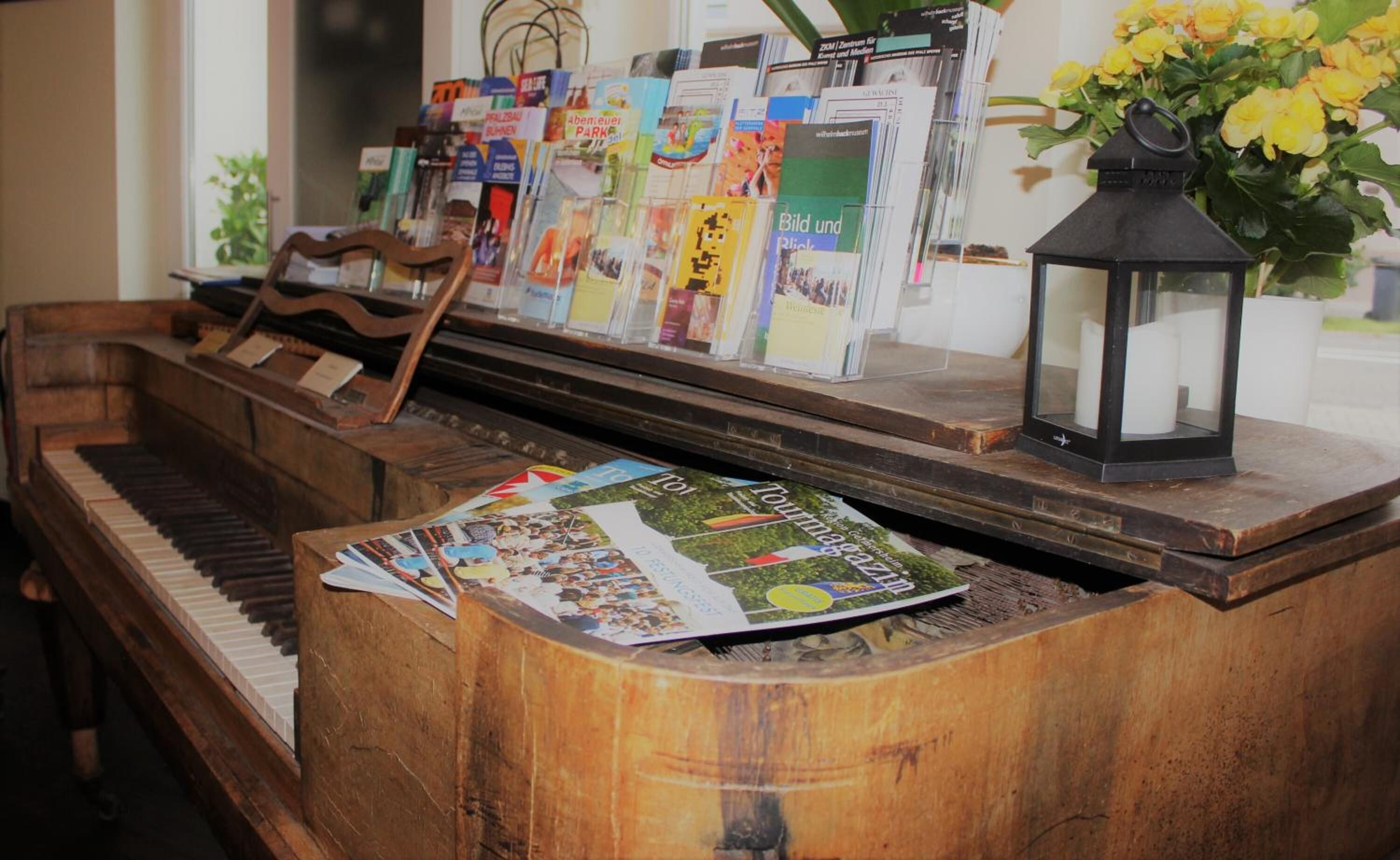 A wooden piano with a magazine on top, a stack of books, and a lantern on a table.