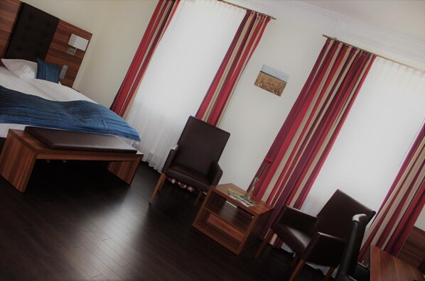 A hotel room with a bed, a wooden bench, a chair, and a small table. - Hotel Germersheimer Hof (Germersheim)