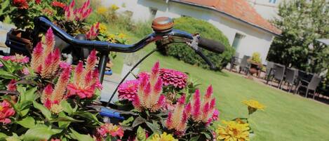 Ein Fahrrad in einem Garten mit bunten Blumen und einem Haus im Hintergrund.