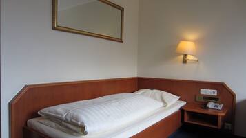 Una cama individual con cabecera de madera, una mesita de noche con lámpara y un teléfono.