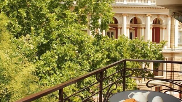 Un balcón con una mesa dispuesta para el té, con vista a un edificio con una cúpula grande y columnas.