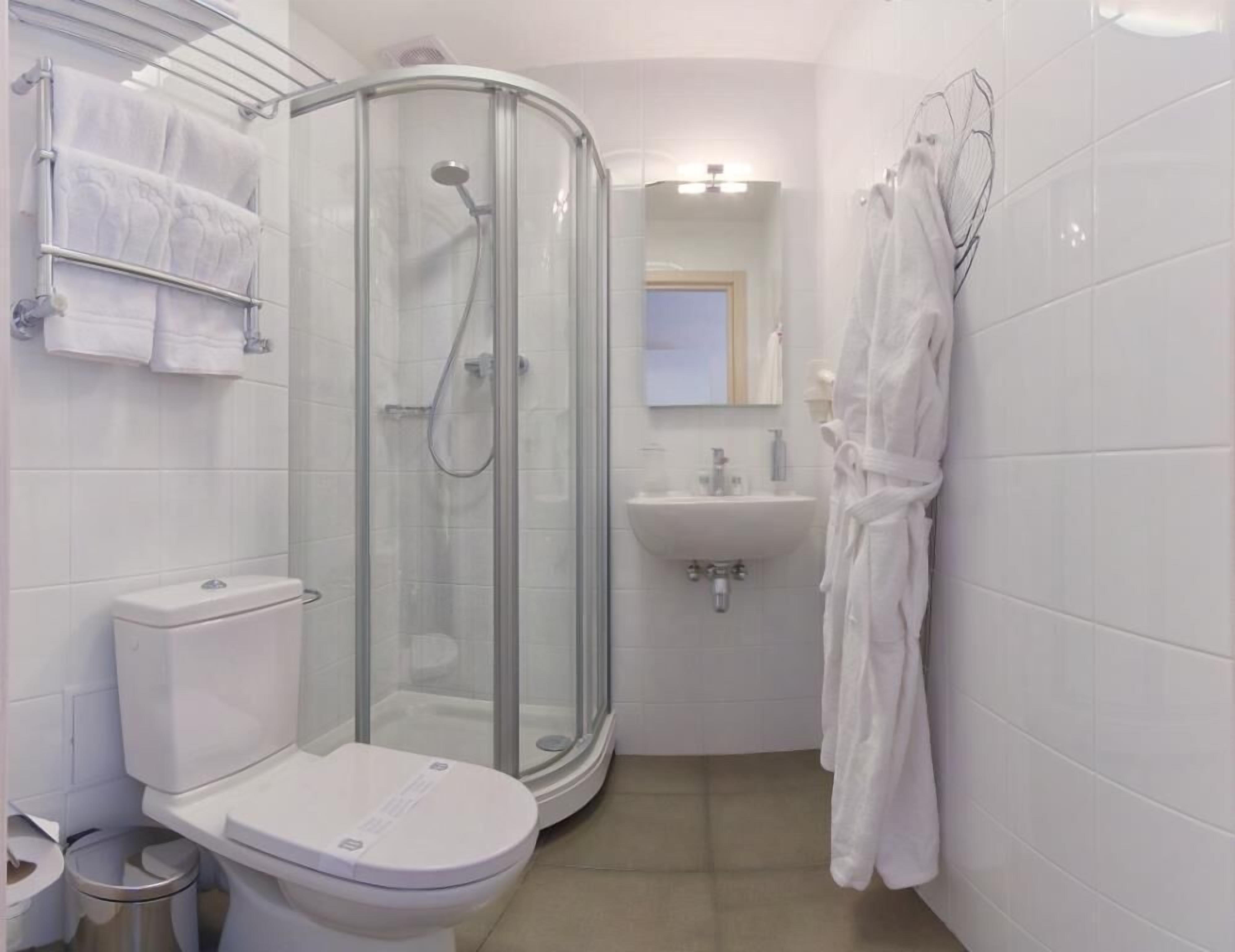Moderni kylpyhuone, jossa on lasiseinällä varustettu suihku, wc, pesuallas ja seinälle ripustettu kylpytakki.