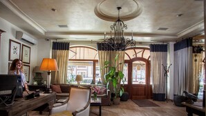 Un vestíbulo espacioso con suelo de madera, un candelabro, un escritorio con ordenador, un sofá y una planta grande en maceta.