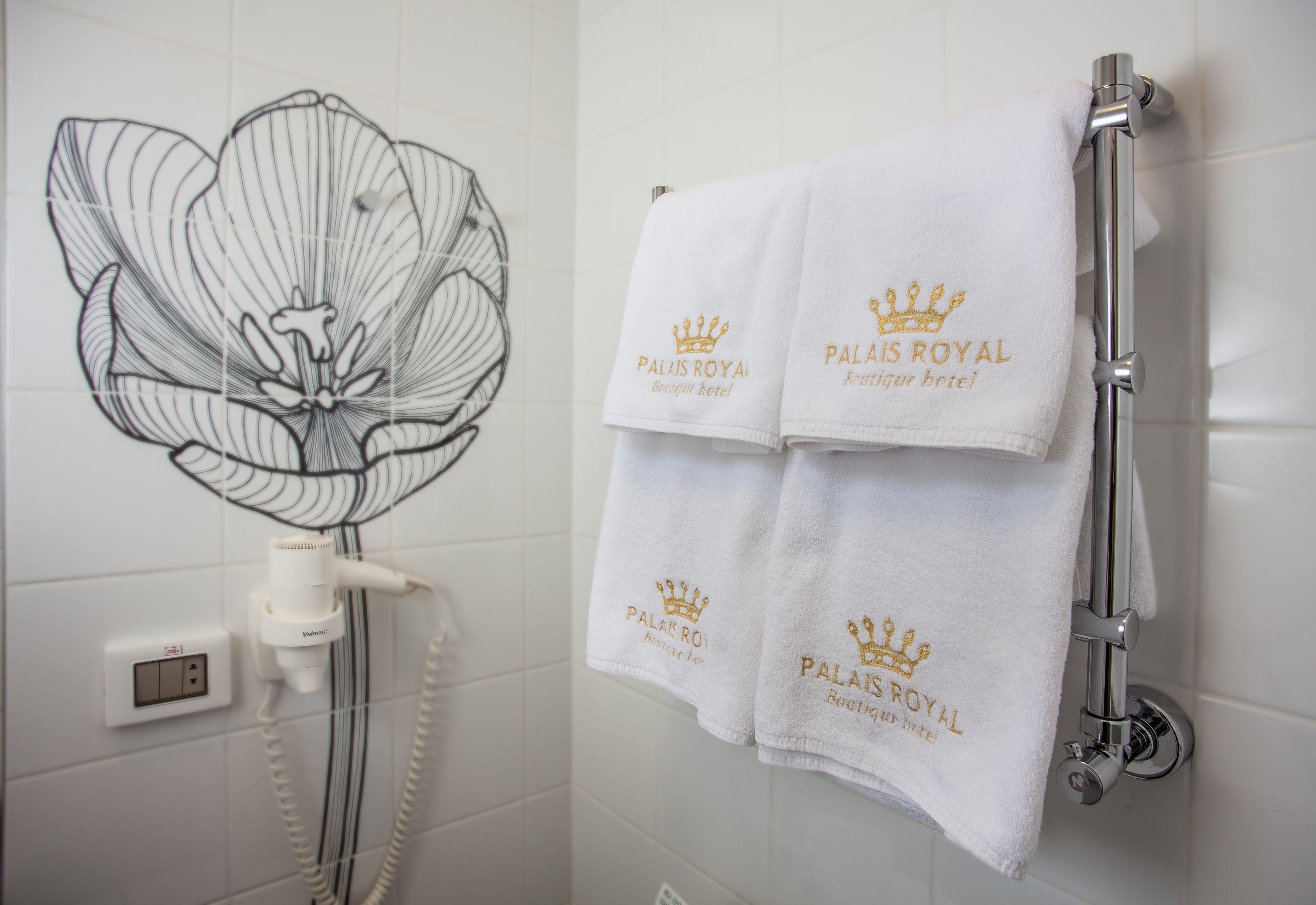 A bathroom with a shower head, a towel rack with two towels, and a wall outlet.