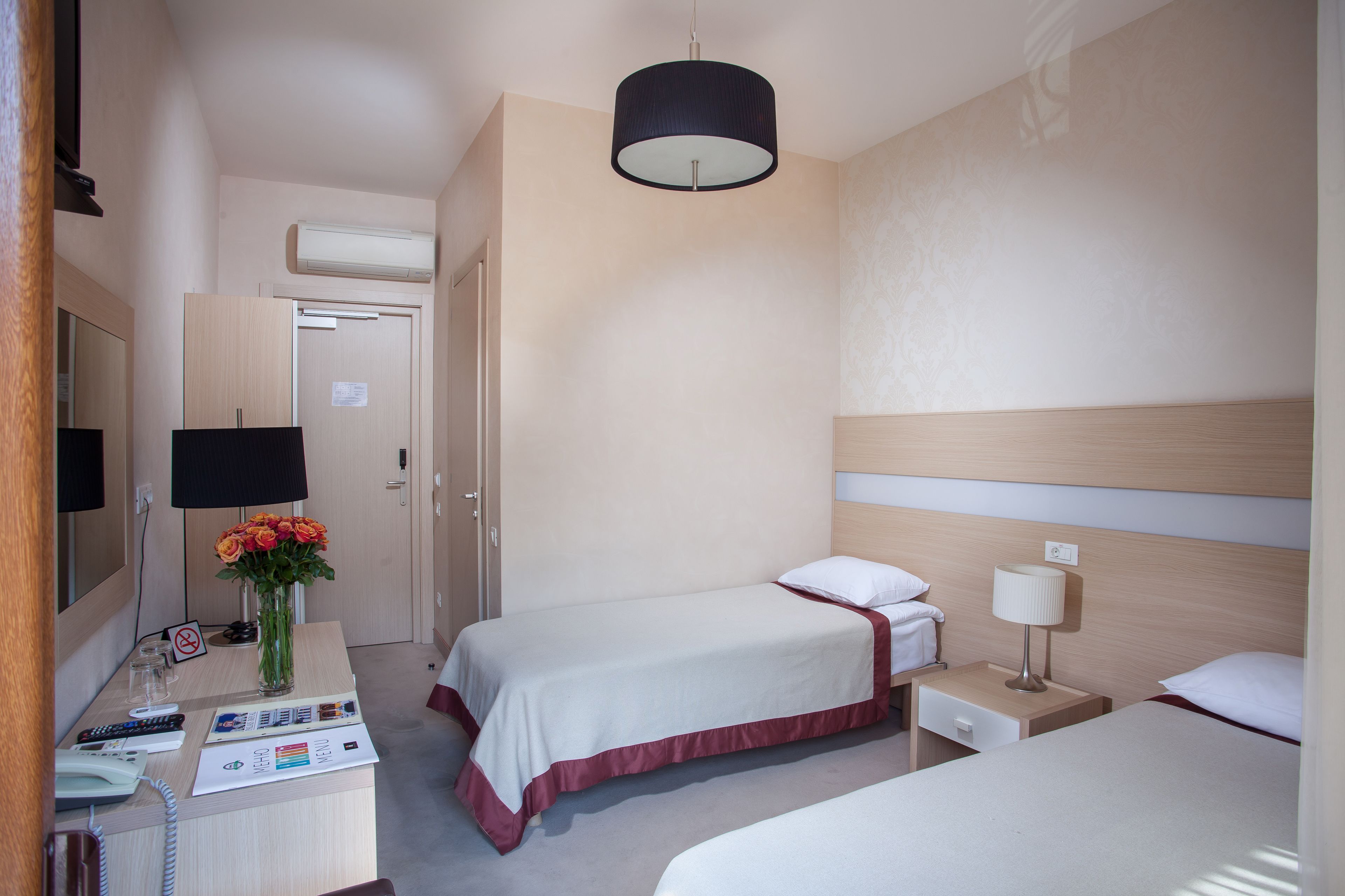 Habitación de hotel con dos camas, un escritorio con teléfono, una lámpara y un florero con flores.