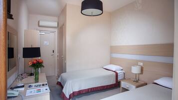 Habitación de hotel con dos camas, un escritorio con teléfono, una lámpara y un florero con flores.