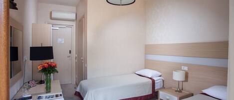 Habitación de hotel con dos camas, un escritorio con teléfono, una lámpara y un florero con flores.