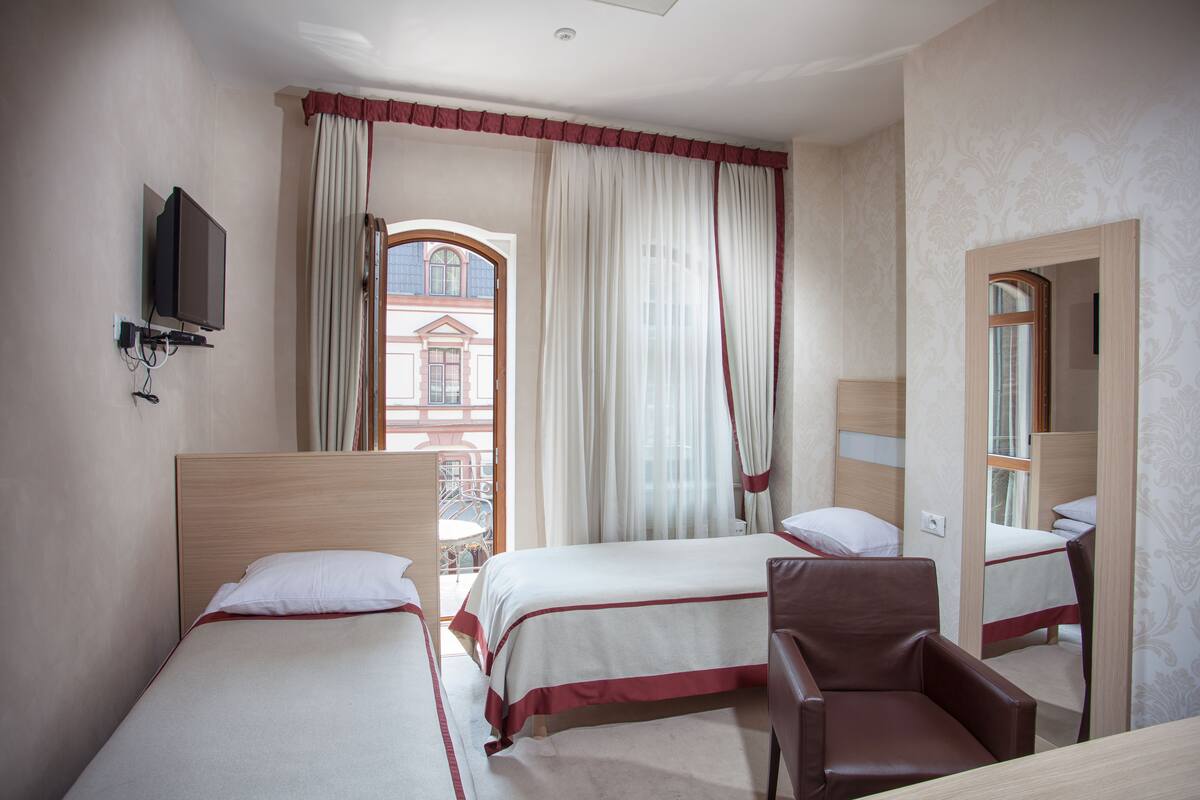 A hotel room with two beds, a chair, a TV, and a window with curtains.