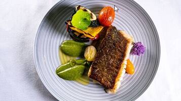 Un plato con un trozo de pescado a la parrilla, tomates cherry y una flor decorativa.