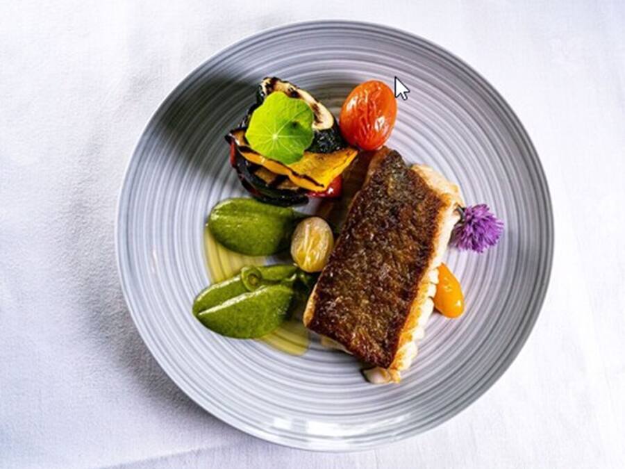 Un plato con un trozo de pescado a la parrilla, tomates cherry y una flor decorativa.