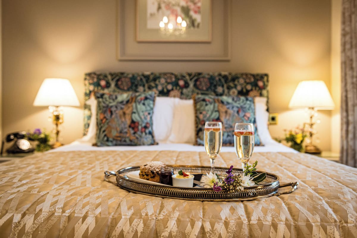 A bed with a tray of food and drinks, a floral headboard, and lamps on either side.
