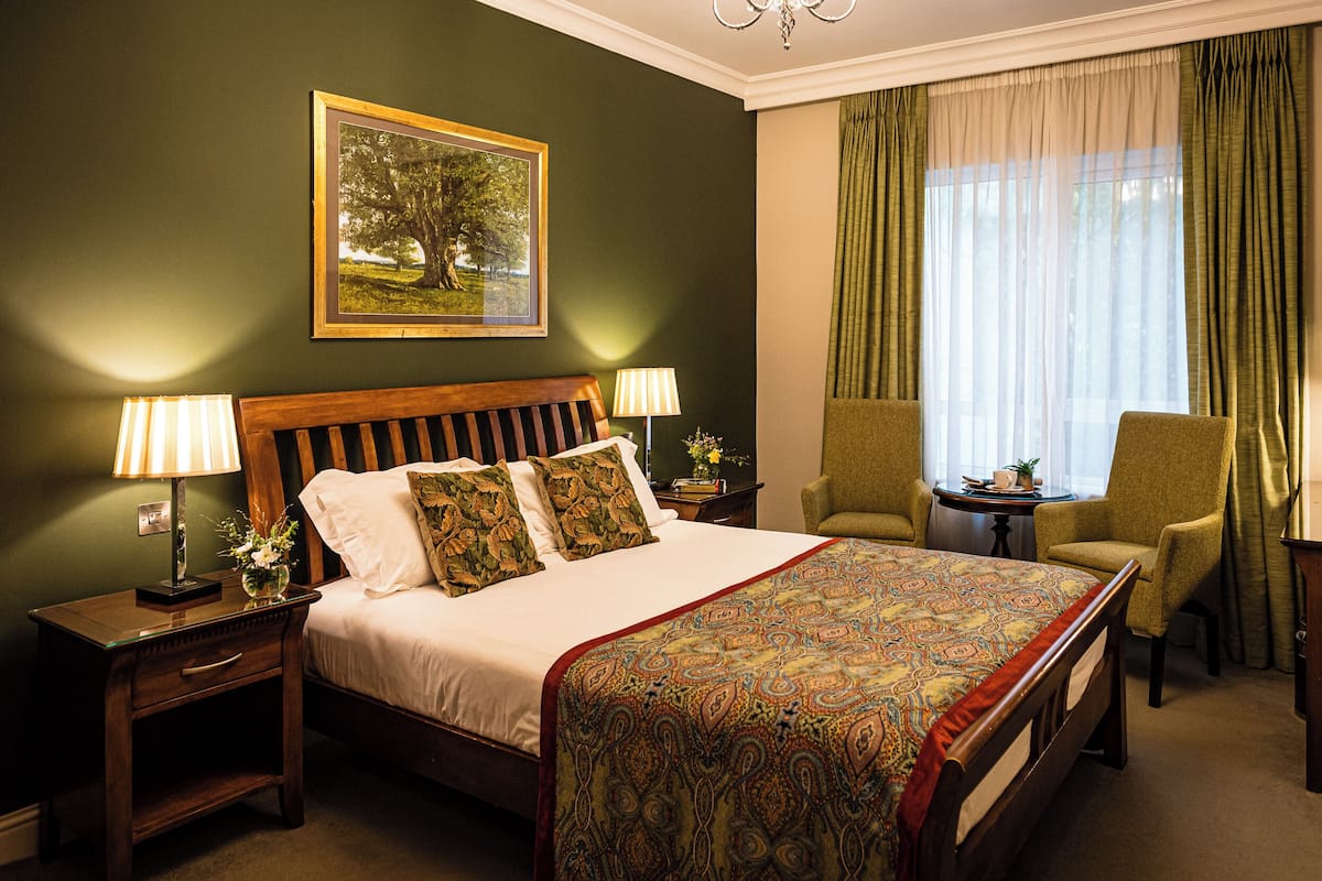 A neatly arranged hotel room with a large bed, two bedside tables with lamps, a chair, and a window with curtains.