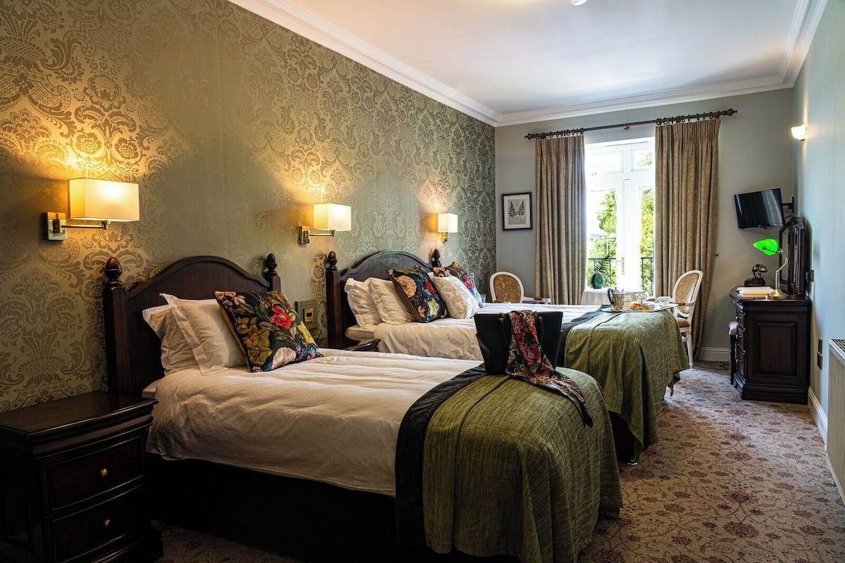 A hotel room with two beds, a desk, a chair, a television, and a window with curtains.