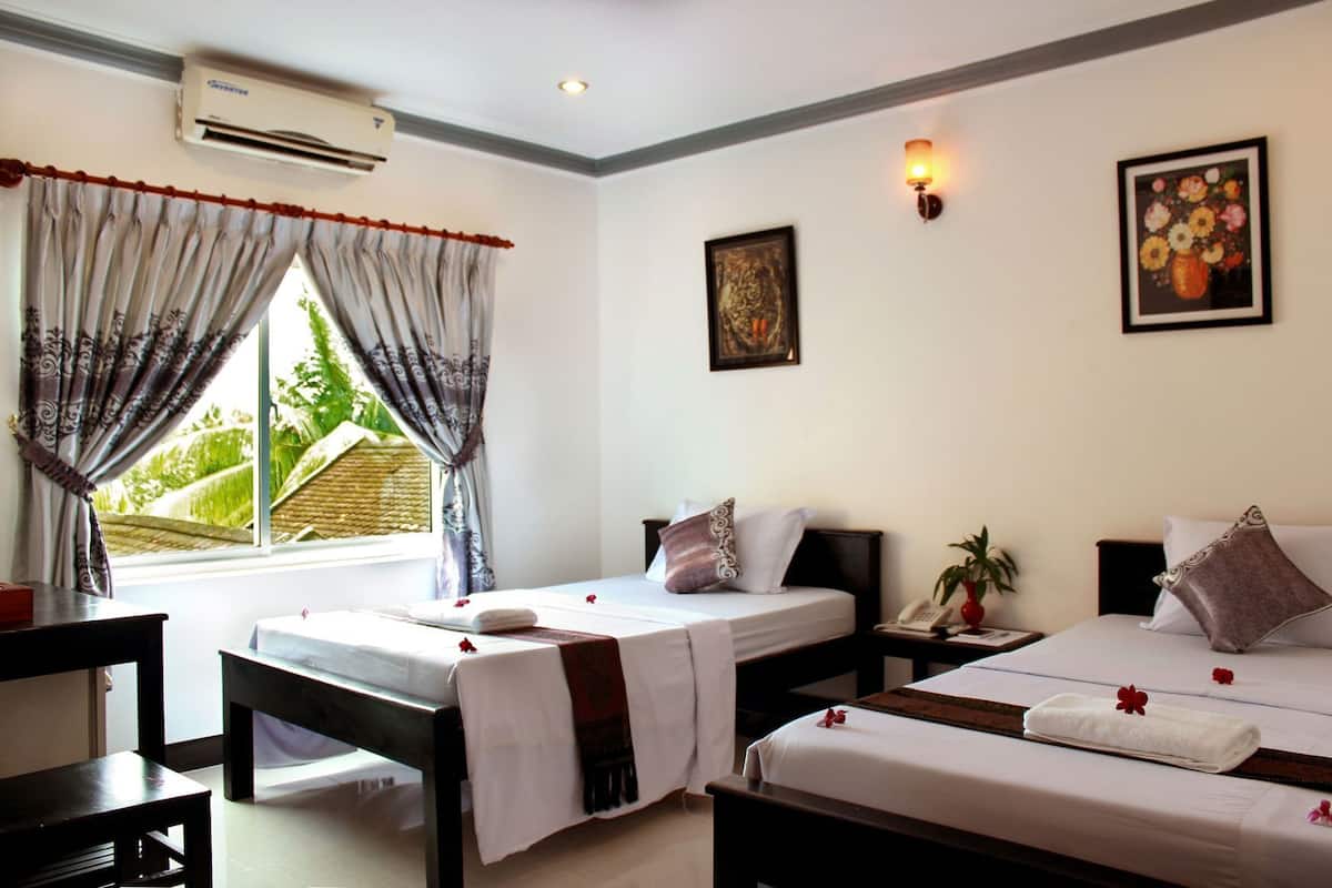 Quarto de hotel com duas camas, uma mesa, ar condicionado, janela com cortinas, telefone fixado na parede e um quadro emoldurado.