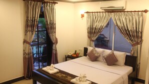 A hotel room with a bed, curtains, a bedside table with a phone and fruit, and an air conditioning unit. - Parent Heritage Angkor Villa (Siem Reap)