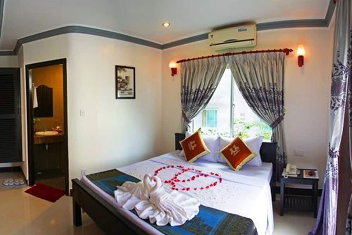 Quarto de hotel com cama bem arrumada, mesa de cabeceira com abajur, janela com cortinas e ar condicionado na parede.
