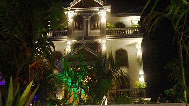 A large, illuminated building with a central tower and balconies, surrounded by tropical foliage. - Parent Heritage Angkor Villa (Siem Reap)
