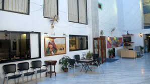 Un vestíbulo de hotel con suelo de mármol, un área de estar con sillas y mesas, y obras de arte en las paredes.