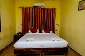 A hotel room with a bed, curtains, a bedside table, and an air conditioner. - Oritel Service Apartments (Mumbai)