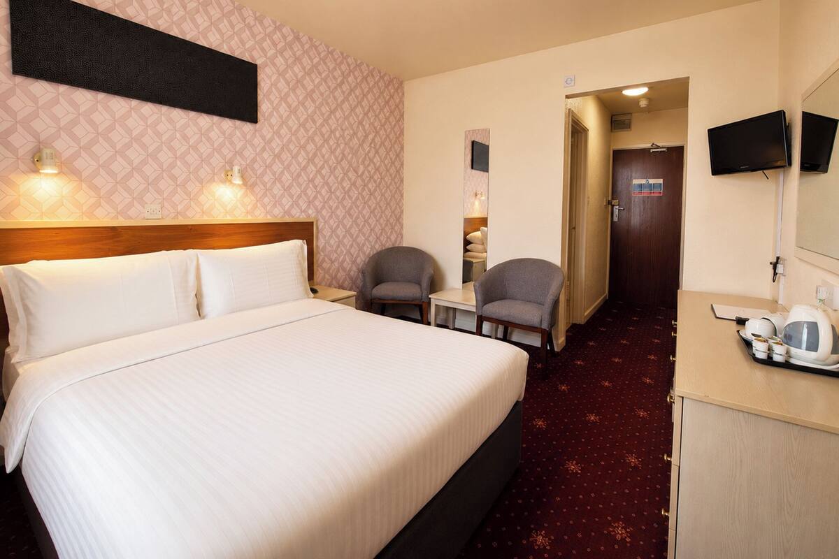 Una habitación de hotel con cama, dos lámparas de noche, una silla, escritorio, televisor y espejo.