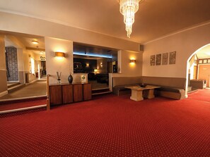 Un hall d’hôtel avec un tapis rouge, un comptoir d’accueil, un espace salon et un lustre.