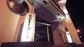 Exterior de un hotel llamado 'NORFOLK' con diseño moderno, destacando una entrada principal y una escalera que conduce a ella.